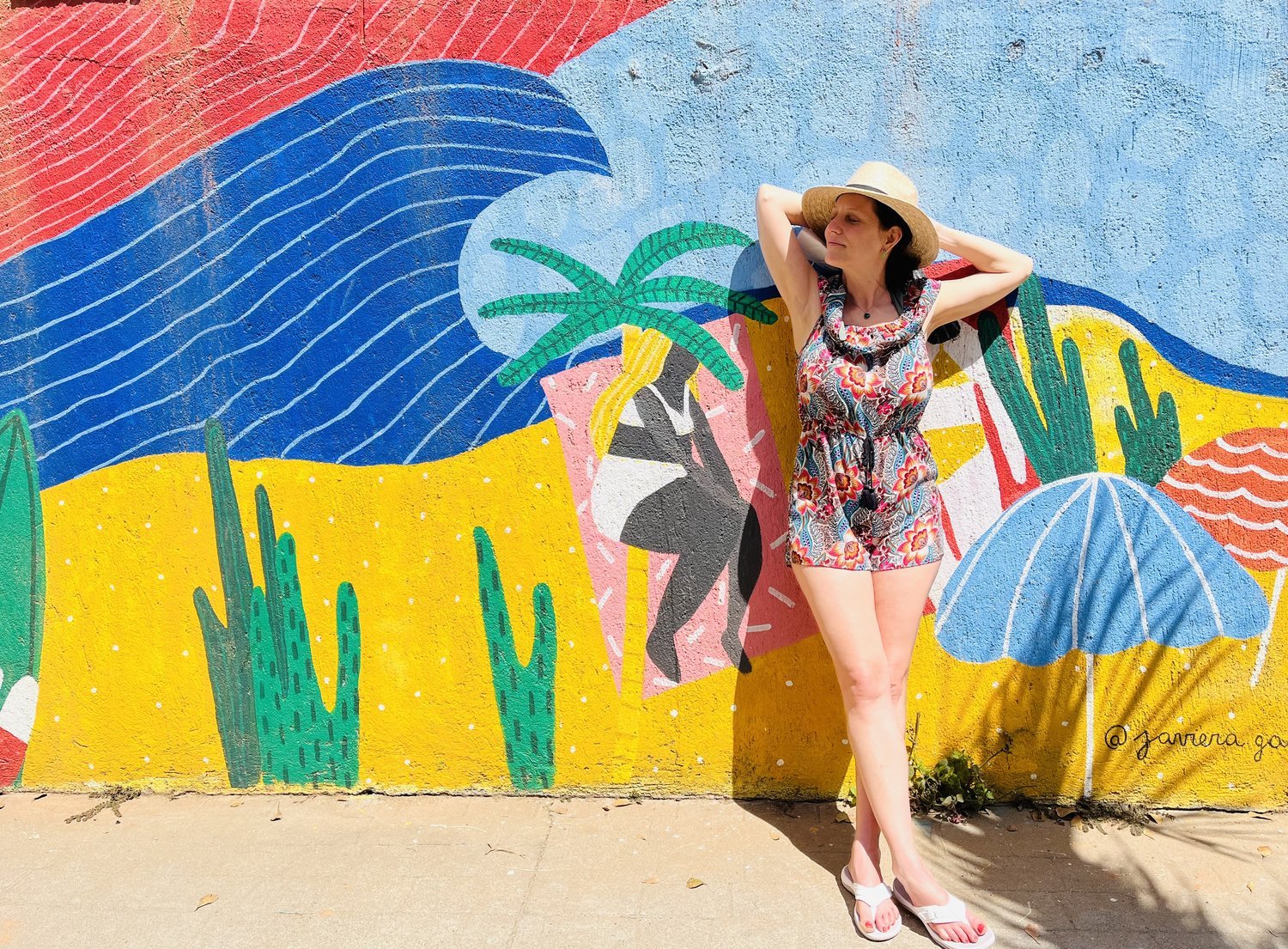 India basking in the sun posed in front a bright, colorful mural of a beach scene in Mexico.
